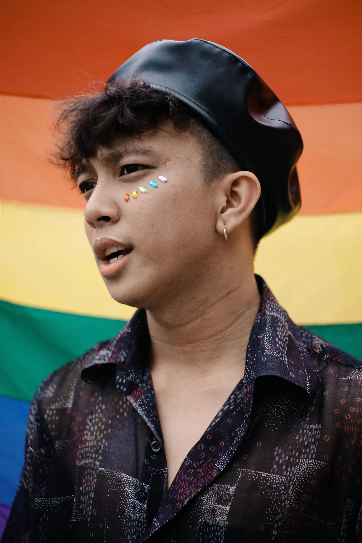 Young adult in a beret in front of a rainbow flag