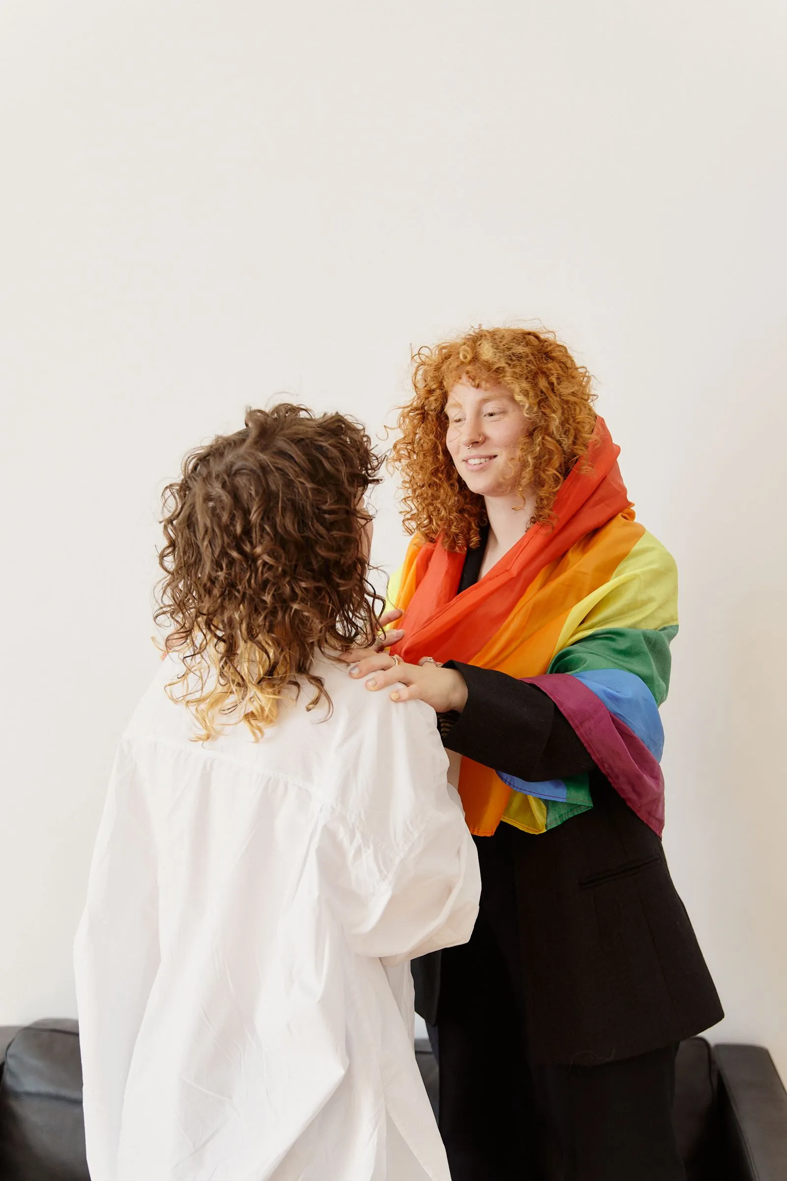 Two people talking together, one with a rainbow pride flag draped over their shoulders